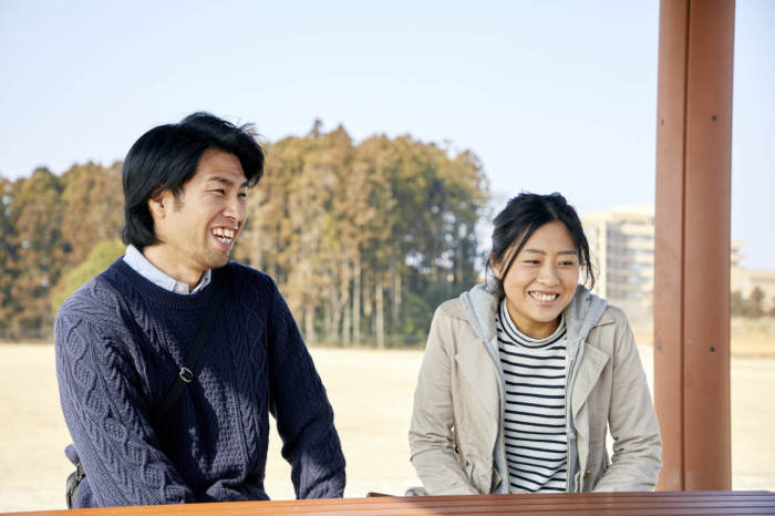 佐藤さんご夫婦が屋外の木製風テーブルを前に座り、笑顔で写っている写真