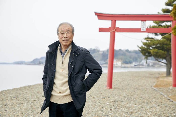 水辺の赤い鳥居の前に立っている青山さんの写真