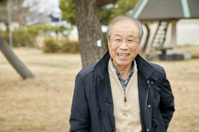 砂地の木の前で笑顔の青山さんの顔写真