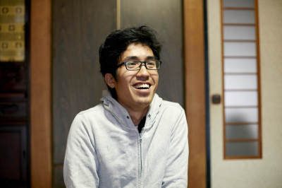 室内に座り、笑顔の村田さんの写真