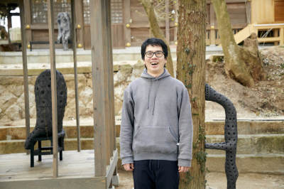 屋外の木の前で笑顔で立っている浅野さんの写真